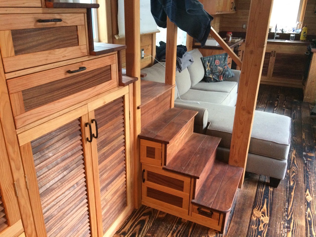 Custom staircase with built-in drawers leading to a loft sofa in a tiny home interior