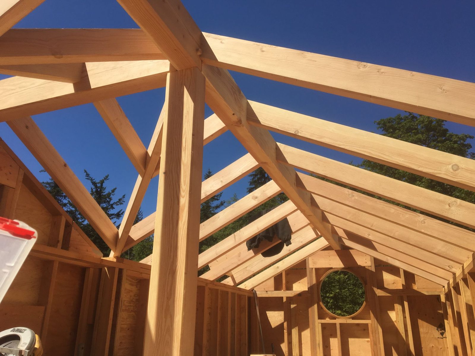 Timber frame and rafter roof structure of a tiny home under construction against blue sky on Quadra Island