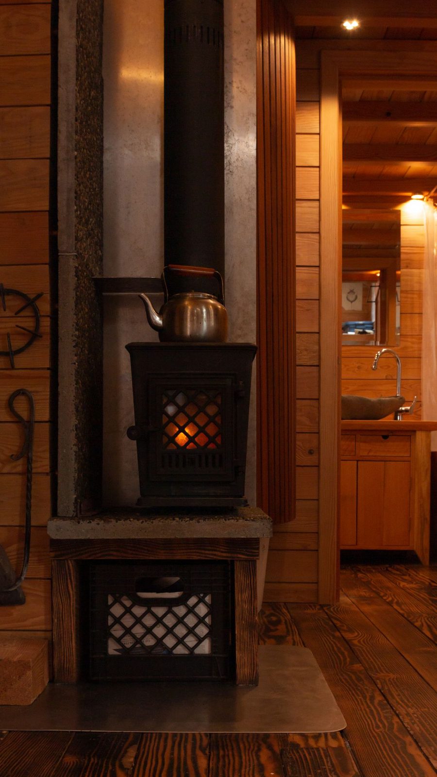 Cast iron wood stove with copper kettle on a tiled hearth beside a kitchen in a tiny home